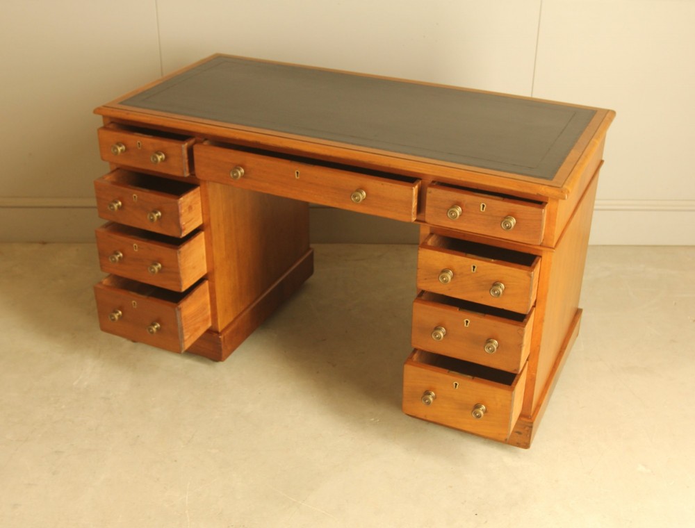 An Edwardian walnut twin-pedestal writing desk featuring nine drawers with circular brass knobs, a dark inset top, and castors mounted on plinth bases. View VII