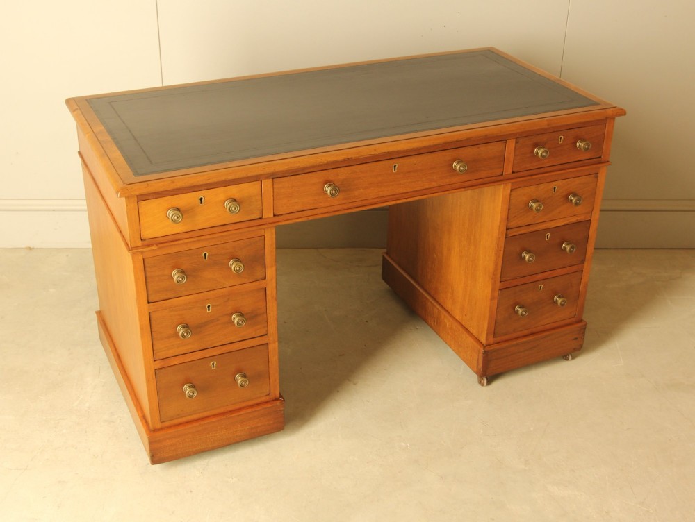 An Edwardian walnut twin-pedestal writing desk featuring nine drawers with circular brass knobs, a dark inset top, and castors mounted on plinth bases. View VIII