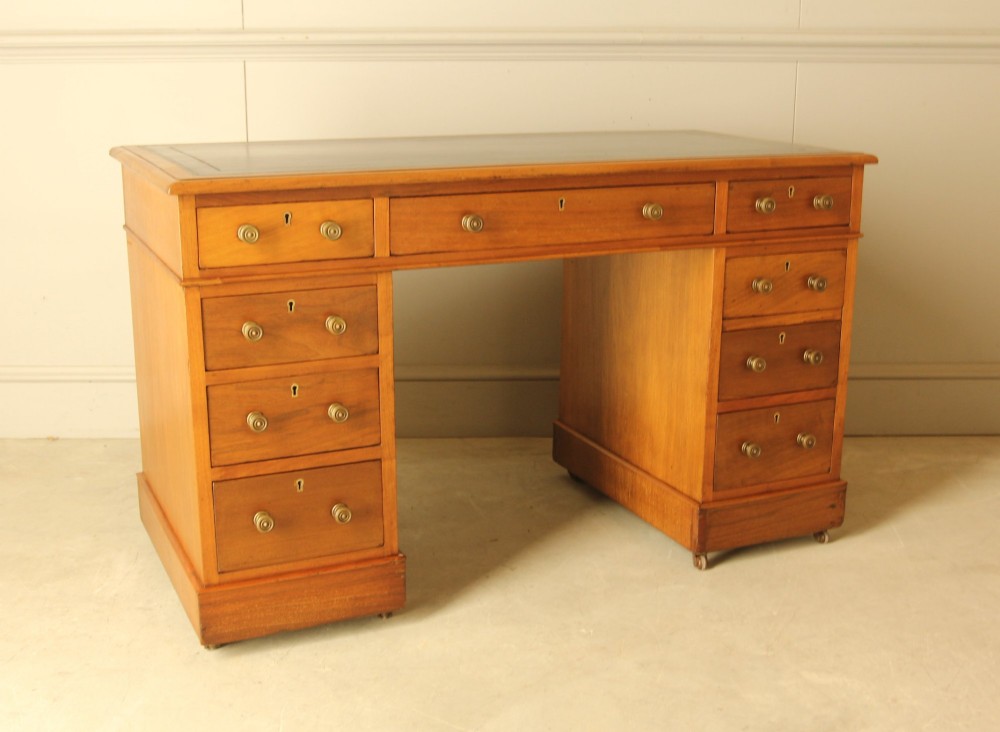 An Edwardian walnut twin-pedestal writing desk featuring nine drawers with circular brass knobs, a dark inset top, and castors mounted on plinth bases. View IX