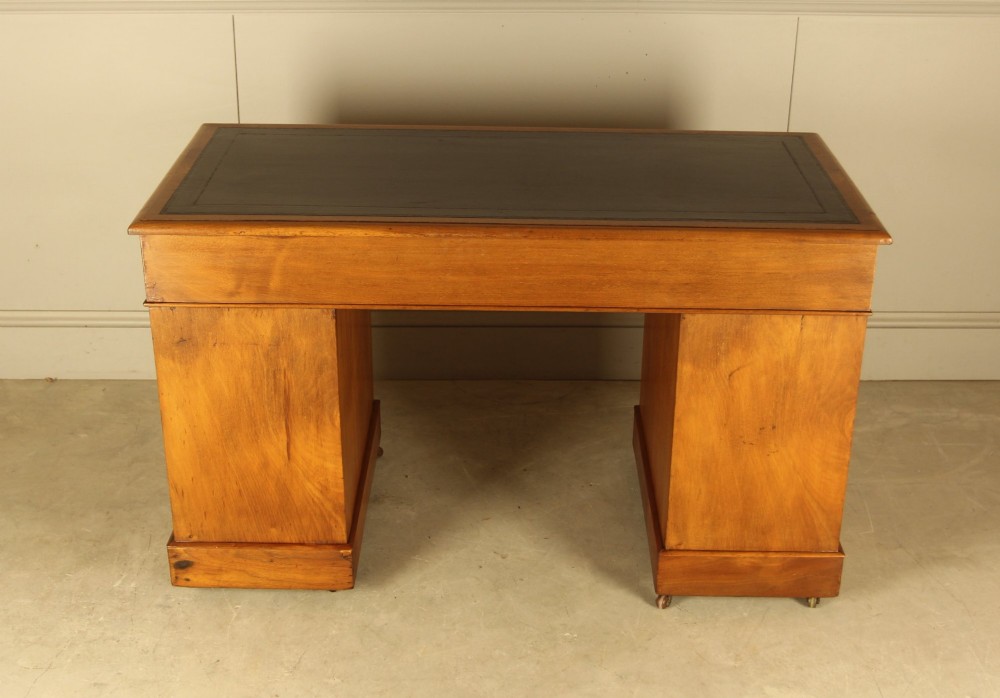An Edwardian walnut twin-pedestal writing desk featuring nine drawers with circular brass knobs, a dark inset top, and castors mounted on plinth bases. View X