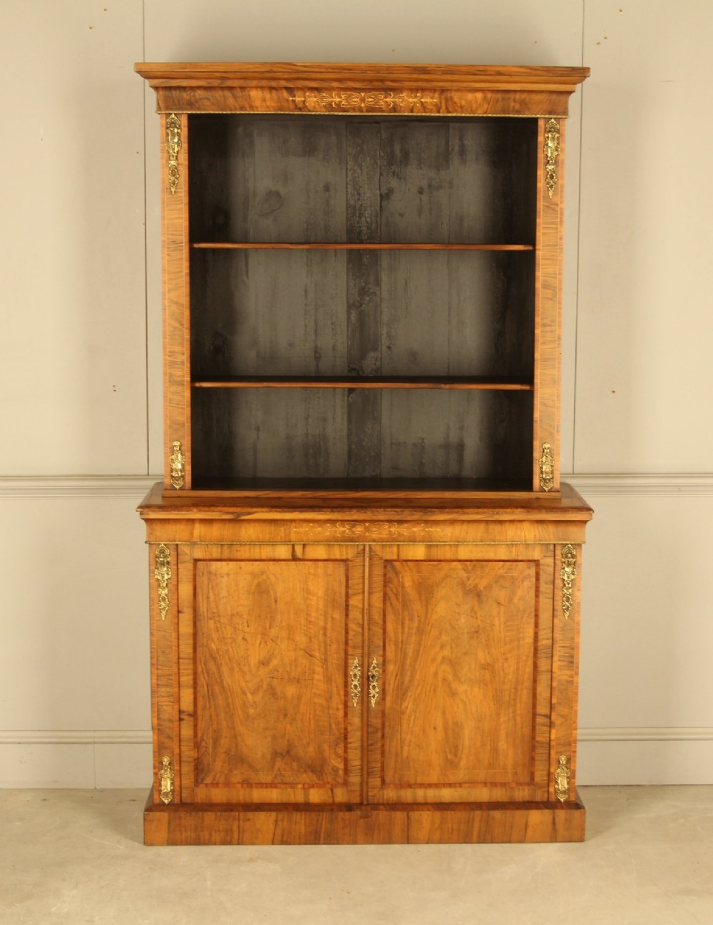 A 19th-century Victorian walnut bookcase featuring an open two-shelf upper section above a two-door lower cupboard with gilt metal mounts and inlaid detailing.