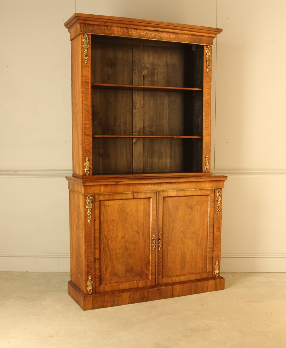 A 19th-century Victorian walnut bookcase featuring an open two-shelf upper section above a two-door lower cupboard with gilt metal mounts and inlaid detailing. View III
