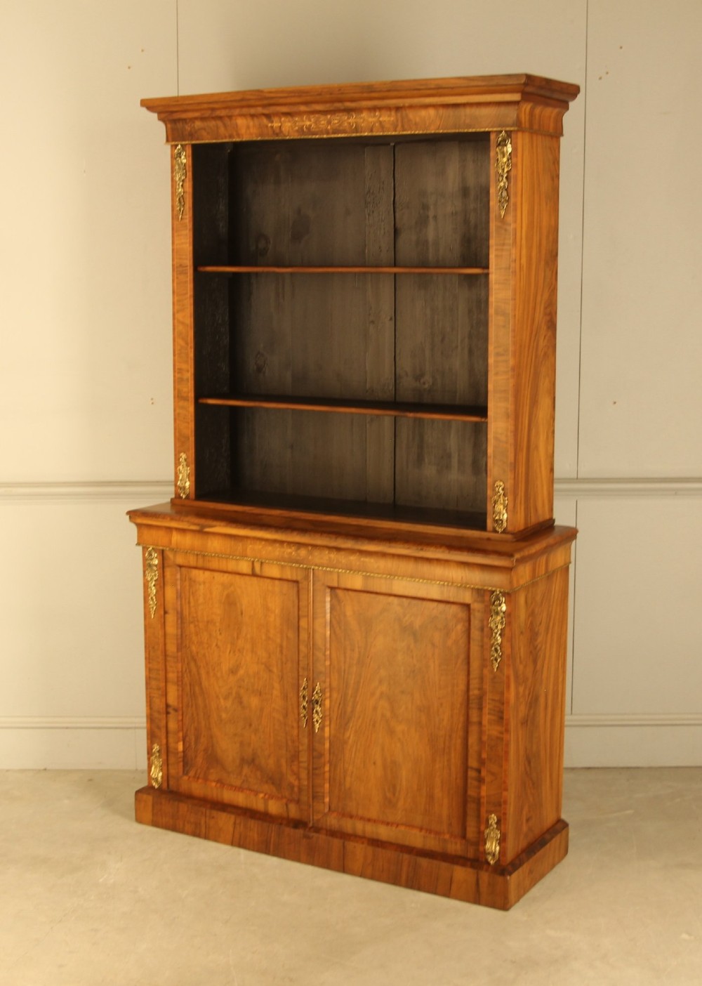 A 19th-century Victorian walnut bookcase featuring an open two-shelf upper section above a two-door lower cupboard with gilt metal mounts and inlaid detailing. View IV
