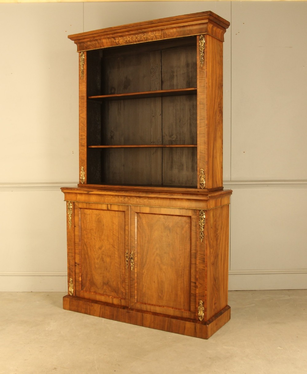 A 19th-century Victorian walnut bookcase featuring an open two-shelf upper section above a two-door lower cupboard with gilt metal mounts and inlaid detailing. View V
