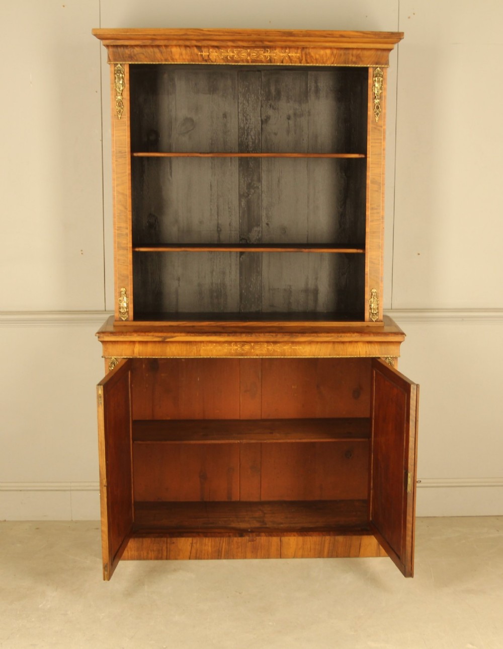 A 19th-century Victorian walnut bookcase featuring an open two-shelf upper section above a two-door lower cupboard with gilt metal mounts and inlaid detailing. View VIII