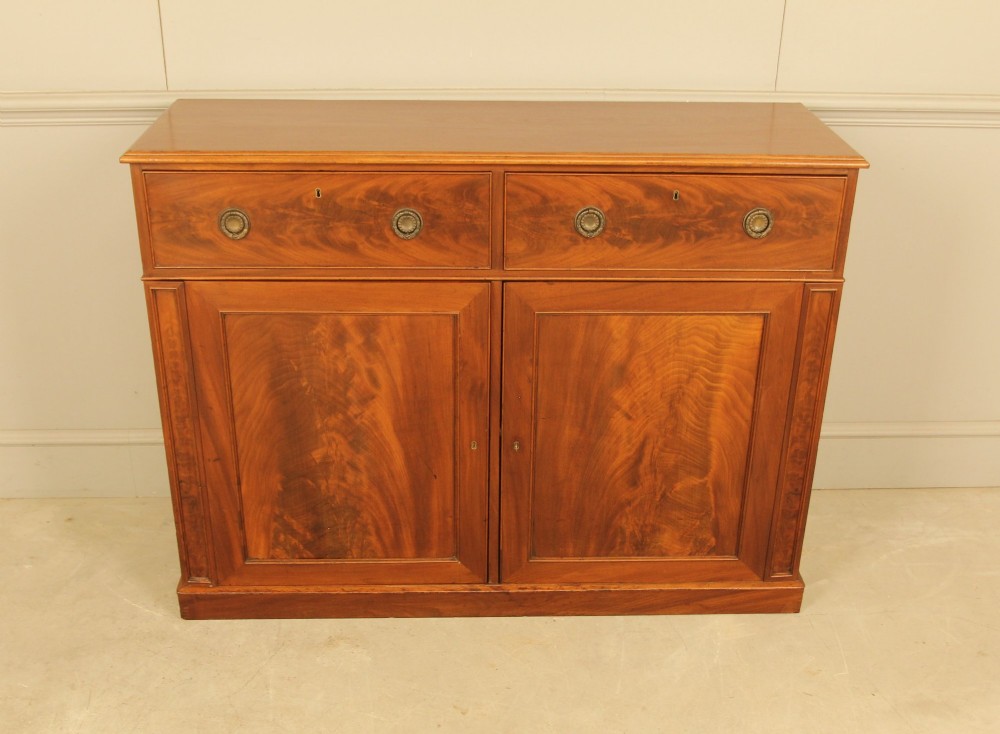 An Edwardian curl mahogany two-door sideboard featuring two top drawers with brass ring handles and panelled cupboard doors on a plinth base. View II