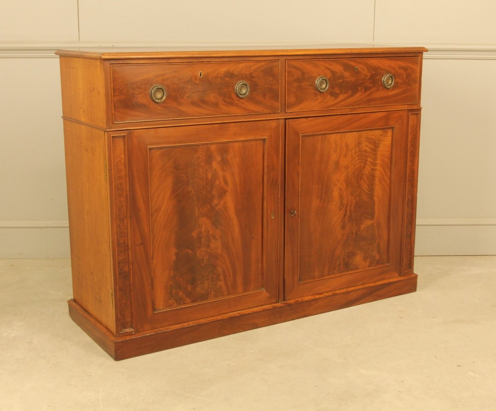 An Edwardian curl mahogany two-door sideboard featuring two top drawers with brass ring handles and panelled cupboard doors on a plinth base. View III