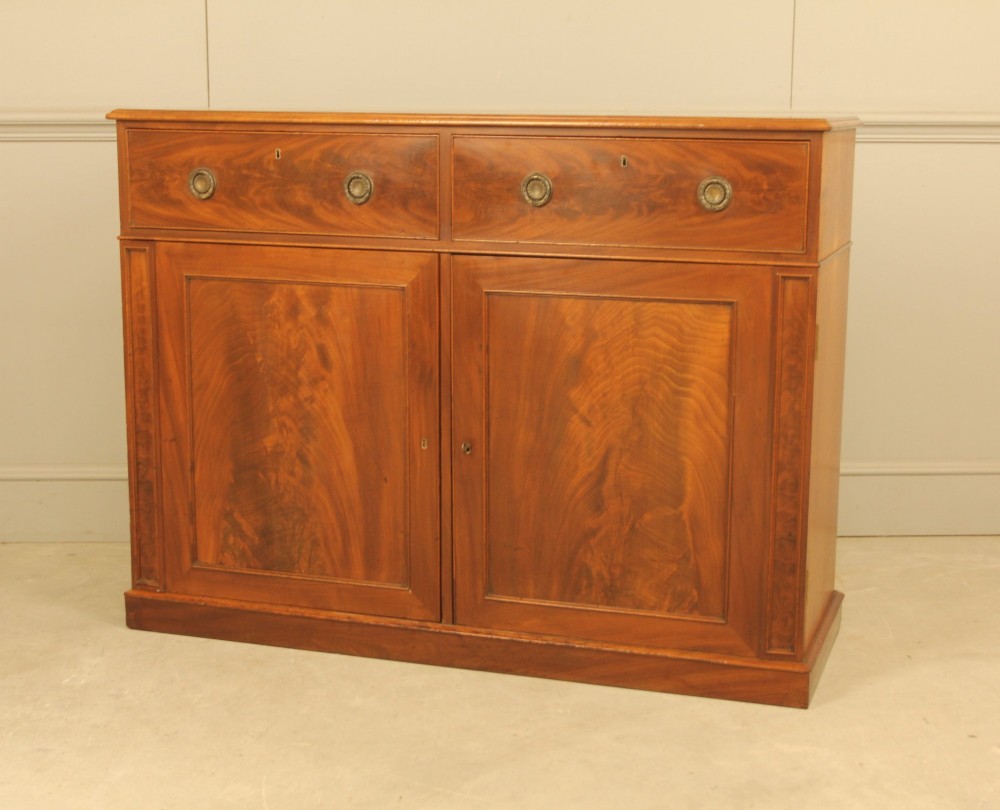 An Edwardian curl mahogany two-door sideboard featuring two top drawers with brass ring handles and panelled cupboard doors on a plinth base. View IV