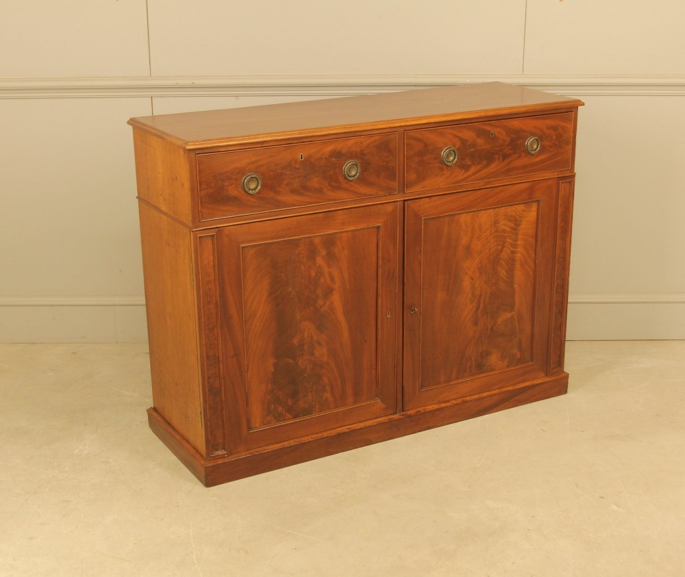 An Edwardian curl mahogany two-door sideboard featuring two top drawers with brass ring handles and panelled cupboard doors on a plinth base. View V