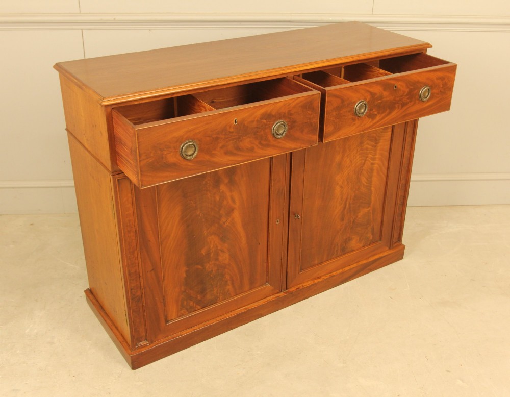 An Edwardian curl mahogany two-door sideboard featuring two top drawers with brass ring handles and panelled cupboard doors on a plinth base. View X