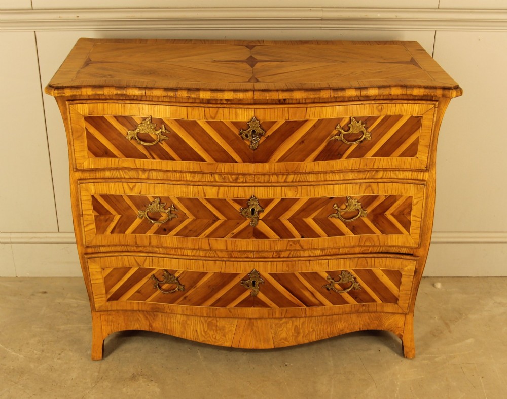 An 18th-century Swedish Rococo bombe chest of drawers featuring geometric chevron parquetry inlays, curved sides, three long drawers, and cast brass hardware. View II