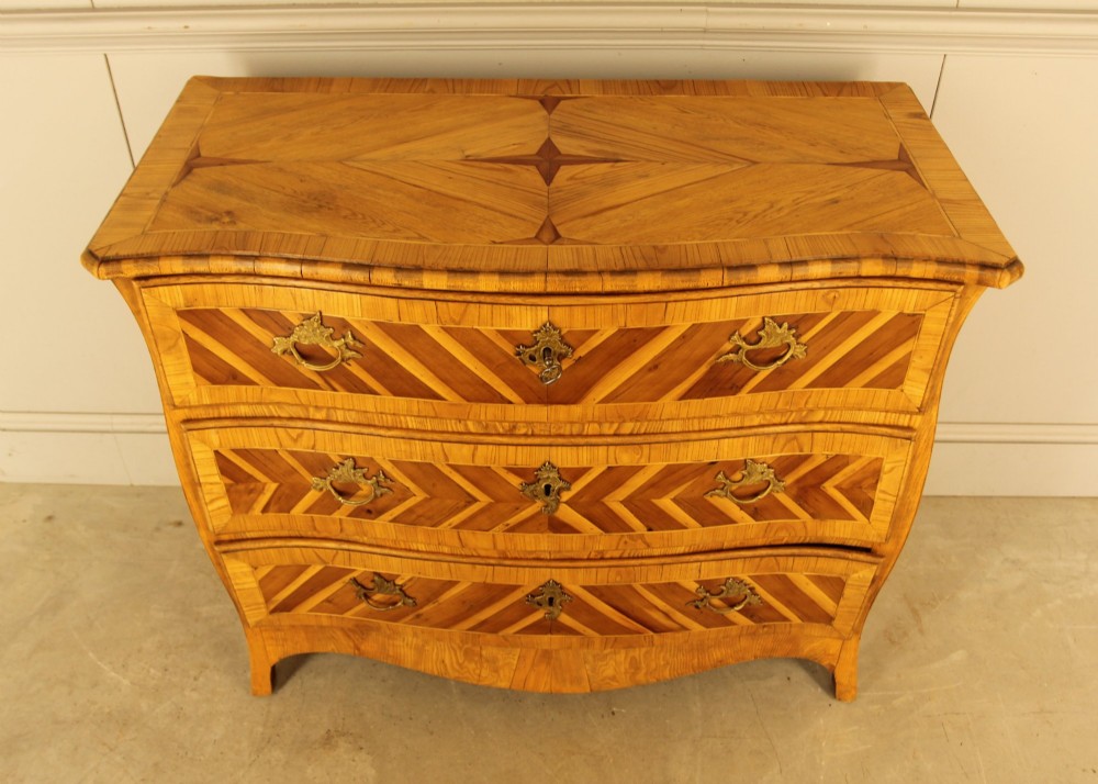 An 18th-century Swedish Rococo bombe chest of drawers featuring geometric chevron parquetry inlays, curved sides, three long drawers, and cast brass hardware. View IV