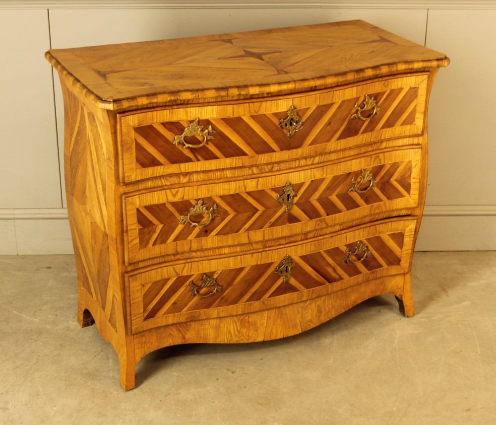 An 18th-century Swedish Rococo bombe chest of drawers featuring geometric chevron parquetry inlays, curved sides, three long drawers, and cast brass hardware. View V