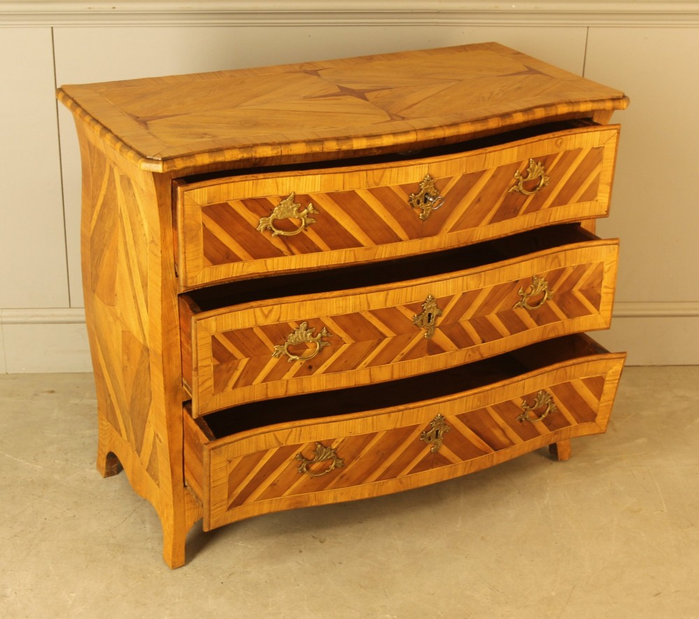 An 18th-century Swedish Rococo bombe chest of drawers featuring geometric chevron parquetry inlays, curved sides, three long drawers, and cast brass hardware. View VI