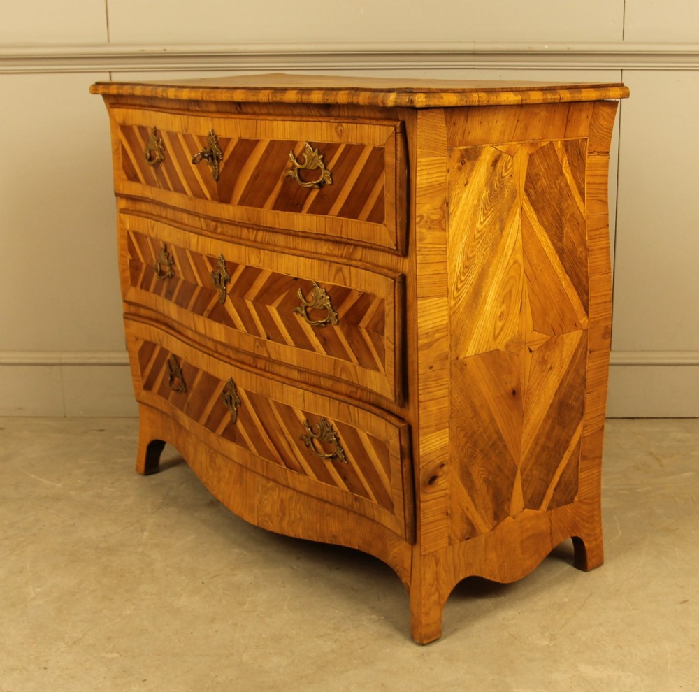 An 18th-century Swedish Rococo bombe chest of drawers featuring geometric chevron parquetry inlays, curved sides, three long drawers, and cast brass hardware. View IX