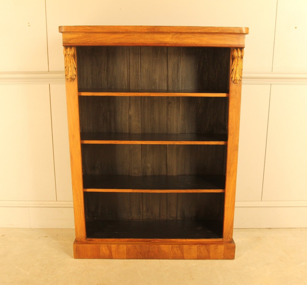 A Victorian walnut open bookcase featuring four horizontal shelves, carved decorative corbels at the upper corners, and a dark painted backboard.
