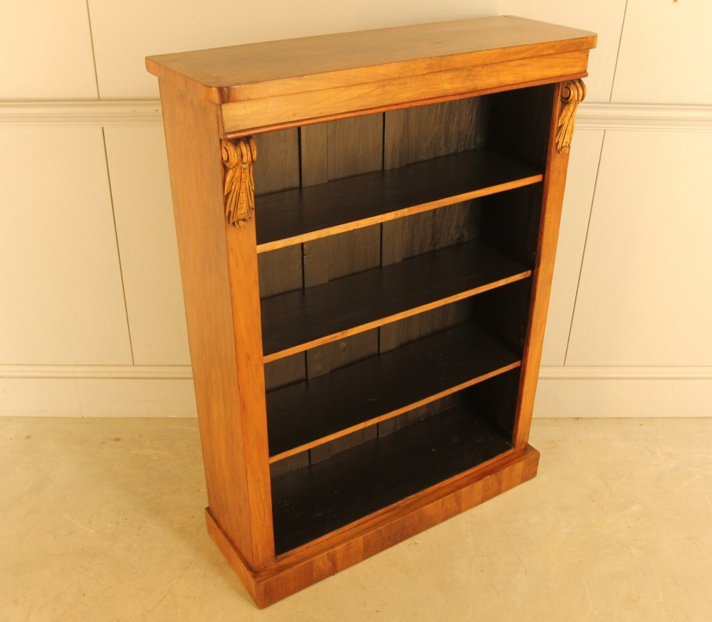 A Victorian walnut open bookcase featuring four horizontal shelves, carved decorative corbels at the upper corners, and a dark painted backboard. View VI