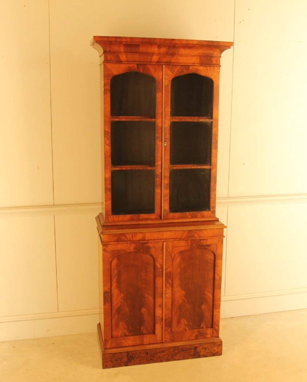 A two-door 19th-century mahogany bookcase featuring an upper glazed display section with internal shelves above a lower cabinet with flame mahogany panelled doors. View V