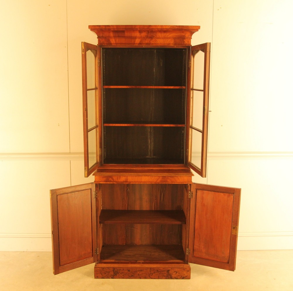 A two-door 19th-century mahogany bookcase featuring an upper glazed display section with internal shelves above a lower cabinet with flame mahogany panelled doors. View VI