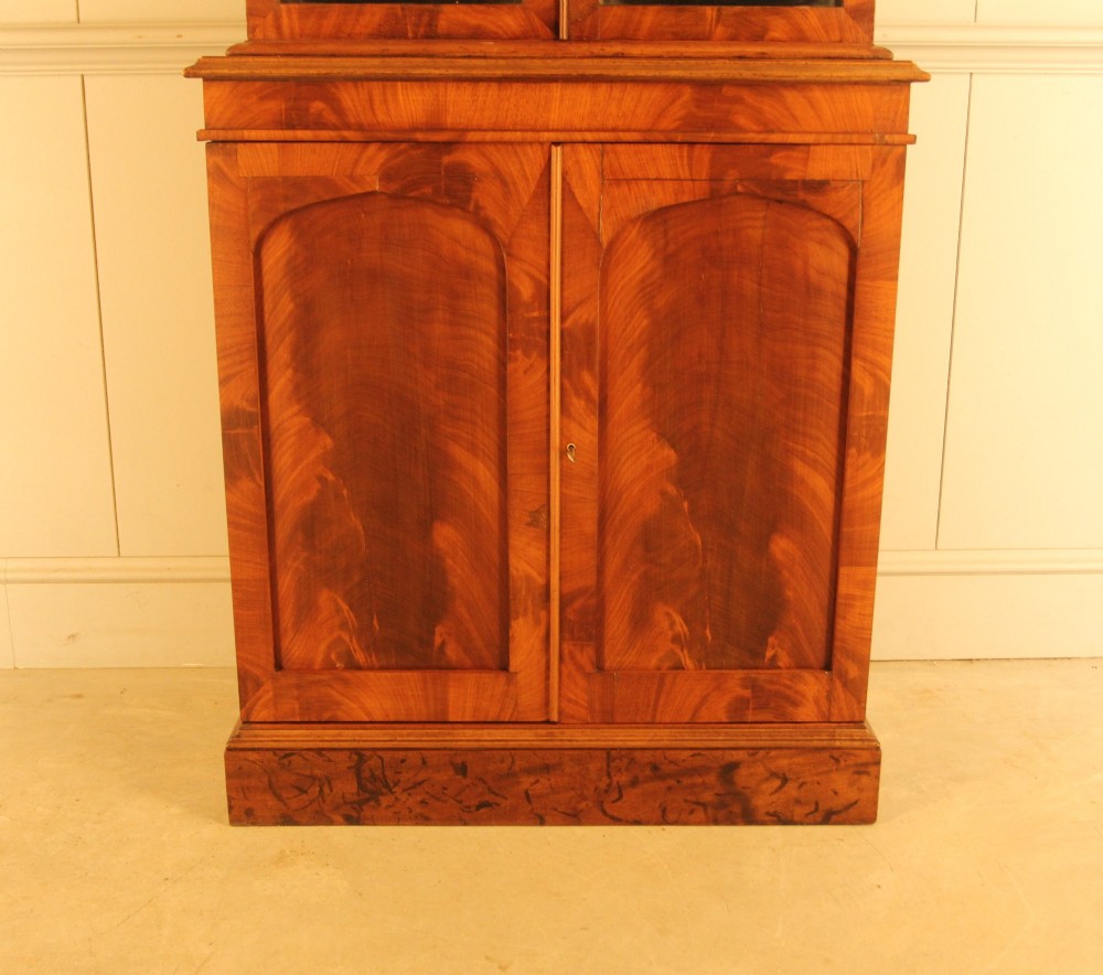 A two-door 19th-century mahogany bookcase featuring an upper glazed display section with internal shelves above a lower cabinet with flame mahogany panelled doors. View VII