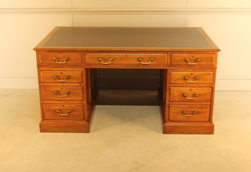 An early 20th-century golden oak twin-pedestal bankers desk featuring a dark leather inset top, nine drawers with brass handles, and panelled sides. View II