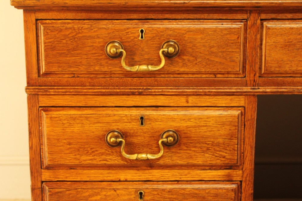 An early 20th-century golden oak twin-pedestal bankers desk featuring a dark leather inset top, nine drawers with brass handles, and panelled sides. View V