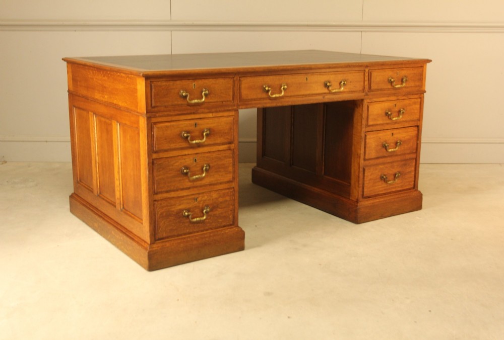 An early 20th-century golden oak twin-pedestal bankers desk featuring a dark leather inset top, nine drawers with brass handles, and panelled sides. View VI