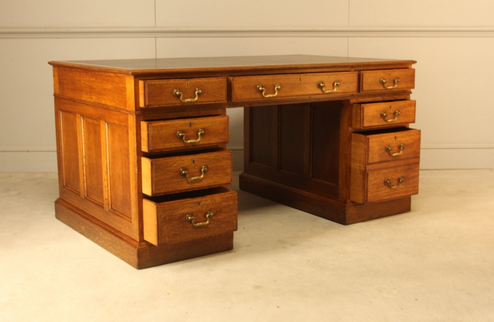An early 20th-century golden oak twin-pedestal bankers desk featuring a dark leather inset top, nine drawers with brass handles, and panelled sides. View VII