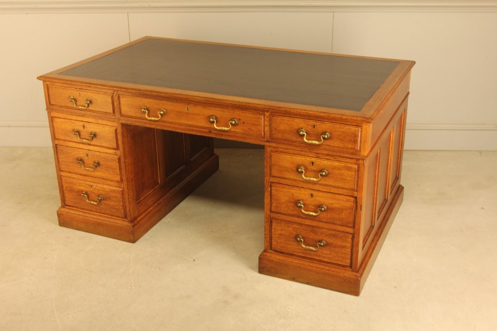 An early 20th-century golden oak twin-pedestal bankers desk featuring a dark leather inset top, nine drawers with brass handles, and panelled sides. View VIII