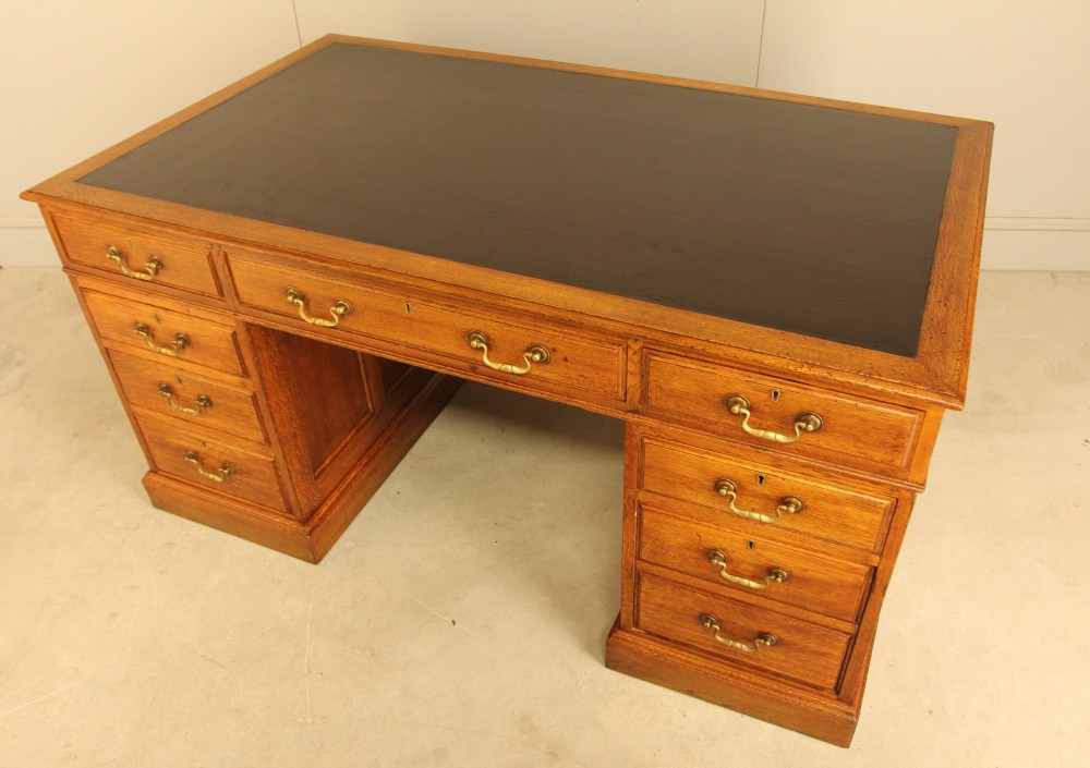 An early 20th-century golden oak twin-pedestal bankers desk featuring a dark leather inset top, nine drawers with brass handles, and panelled sides. View IX