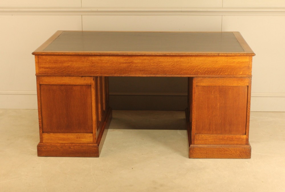 An early 20th-century golden oak twin-pedestal bankers desk featuring a dark leather inset top, nine drawers with brass handles, and panelled sides. View XI