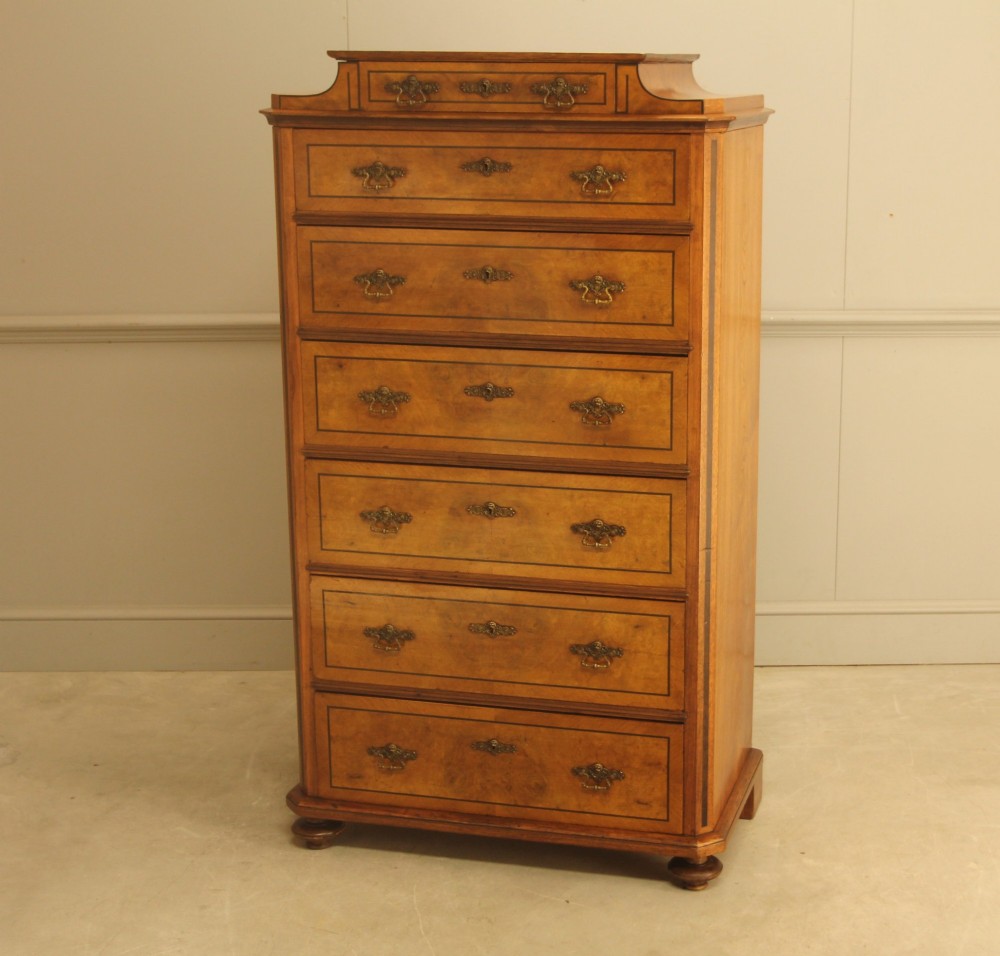 A tall 19th-century Swedish burr walnut chest of drawers featuring seven drawers, crossbanded inlay, ornate brass handles, and a stepped top section. View IV
