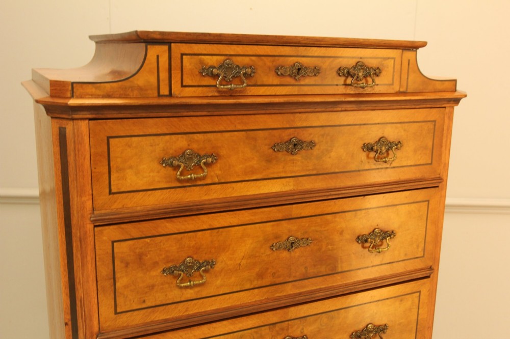 A tall 19th-century Swedish burr walnut chest of drawers featuring seven drawers, crossbanded inlay, ornate brass handles, and a stepped top section. View V