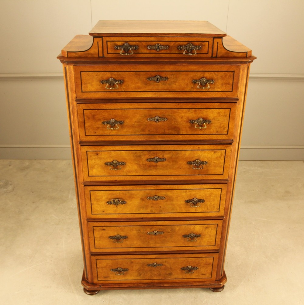 A tall 19th-century Swedish burr walnut chest of drawers featuring seven drawers, crossbanded inlay, ornate brass handles, and a stepped top section. View VI