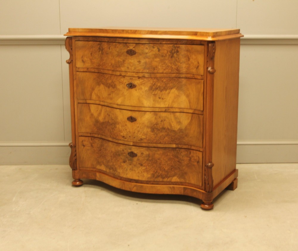 A 19th-century Swedish burr walnut chest of drawers featuring a serpentine front, four graduated drawers, brass escutcheons, and carved side pilasters.