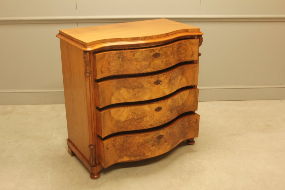 A 19th-century Swedish burr walnut chest of drawers featuring a serpentine front, four graduated drawers, brass escutcheons, and carved side pilasters. View IV