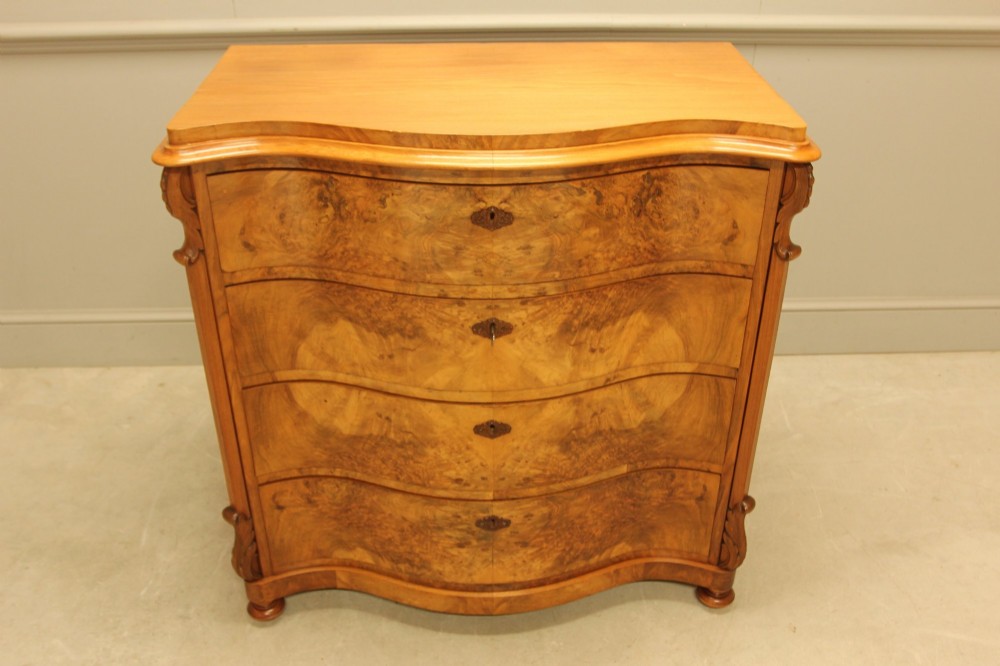 A 19th-century Swedish burr walnut chest of drawers featuring a serpentine front, four graduated drawers, brass escutcheons, and carved side pilasters. View V