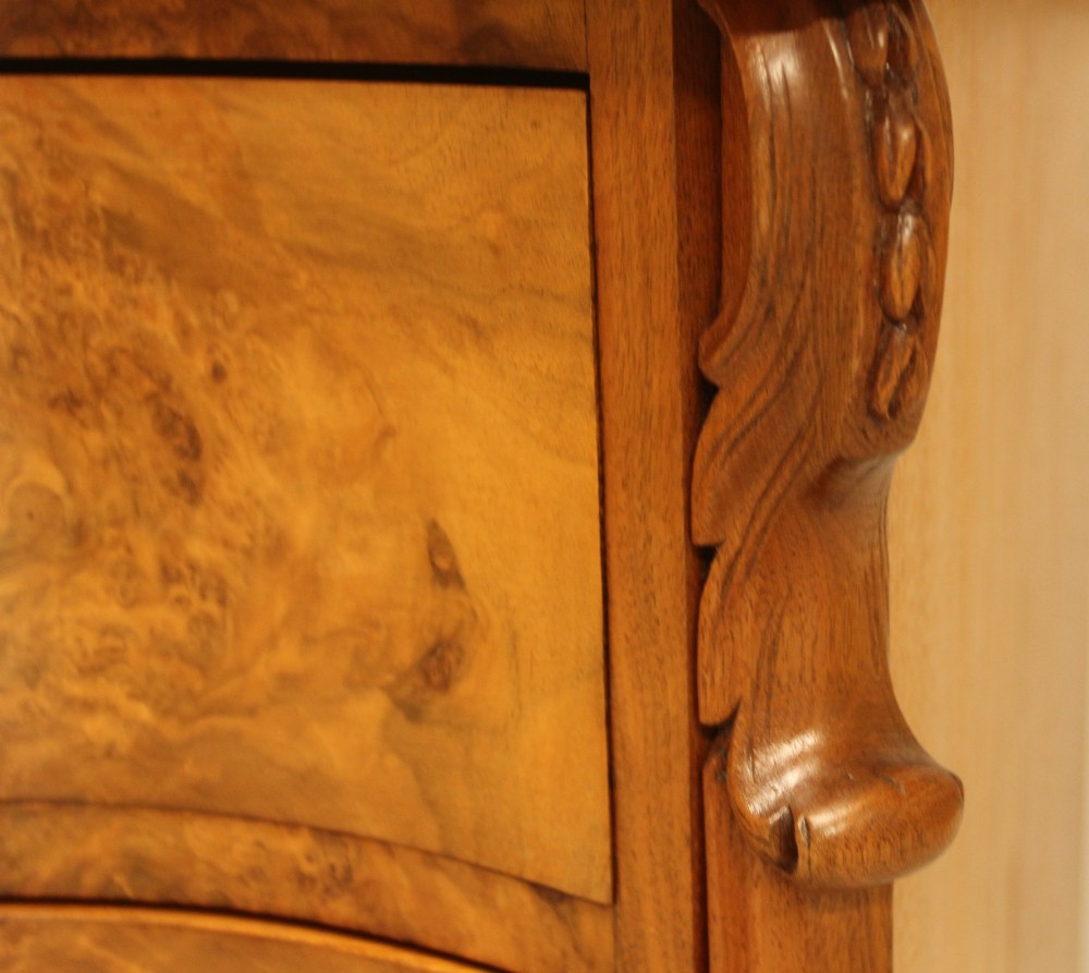 A 19th-century Swedish burr walnut chest of drawers featuring a serpentine front, four graduated drawers, brass escutcheons, and carved side pilasters. View X