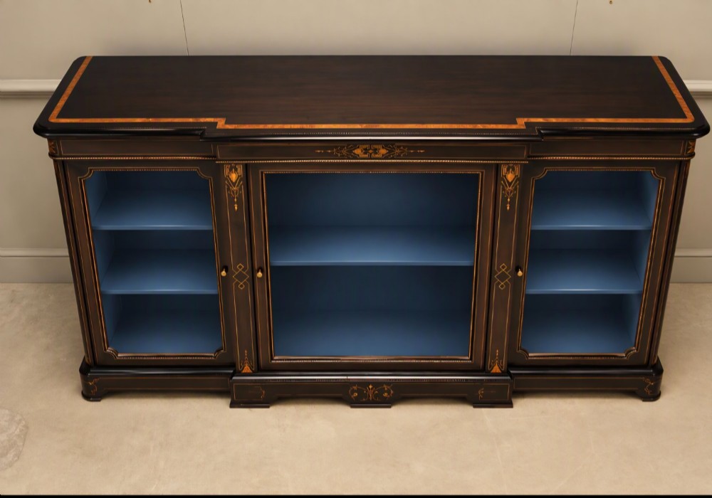 A Victorian ebonised wood breakfront display cabinet featuring three glazed doors, gold inlay detail, and a blue painted interior. View II