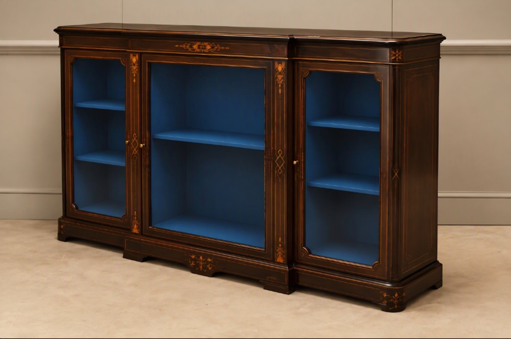 A Victorian ebonised wood breakfront display cabinet featuring three glazed doors, gold inlay detail, and a blue painted interior. View V