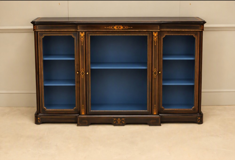 A Victorian ebonised wood breakfront display cabinet featuring three glazed doors, gold inlay detail, and a blue painted interior. View VIII