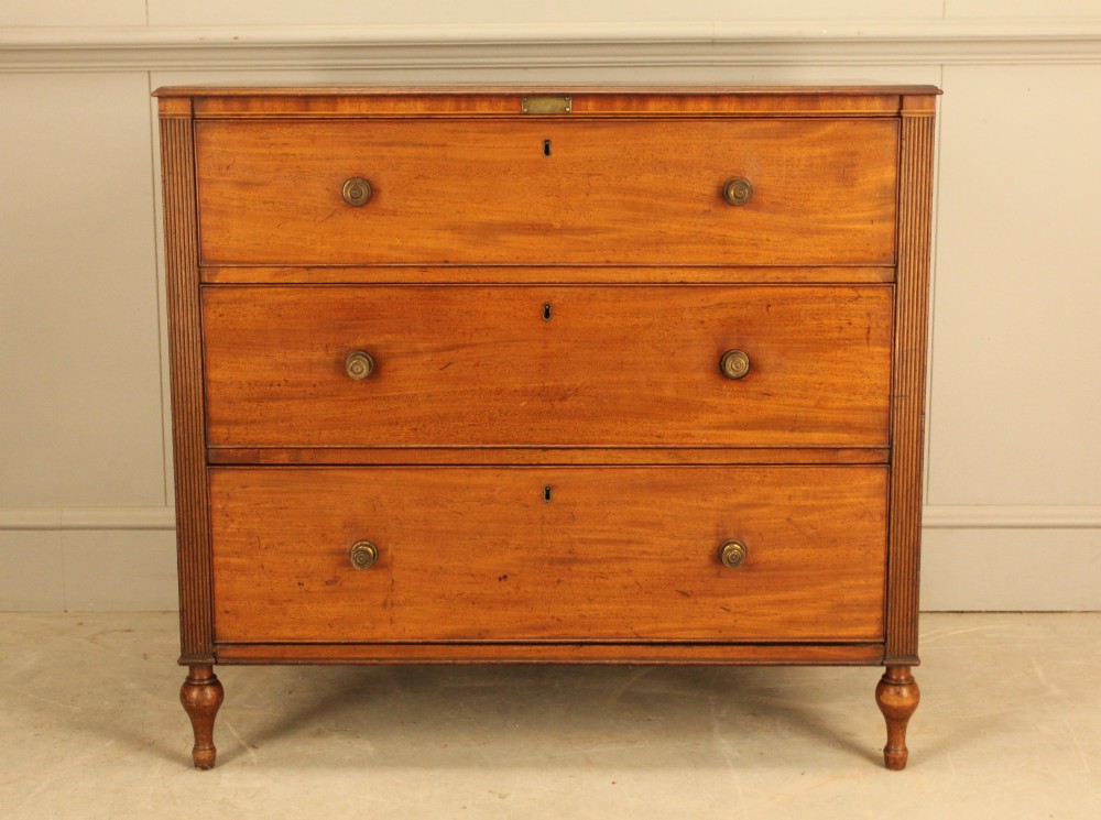 A Regency mahogany chest of drawers featuring three graduated drawers with brass turned knobs and reeded side pilasters resting on turned feet.