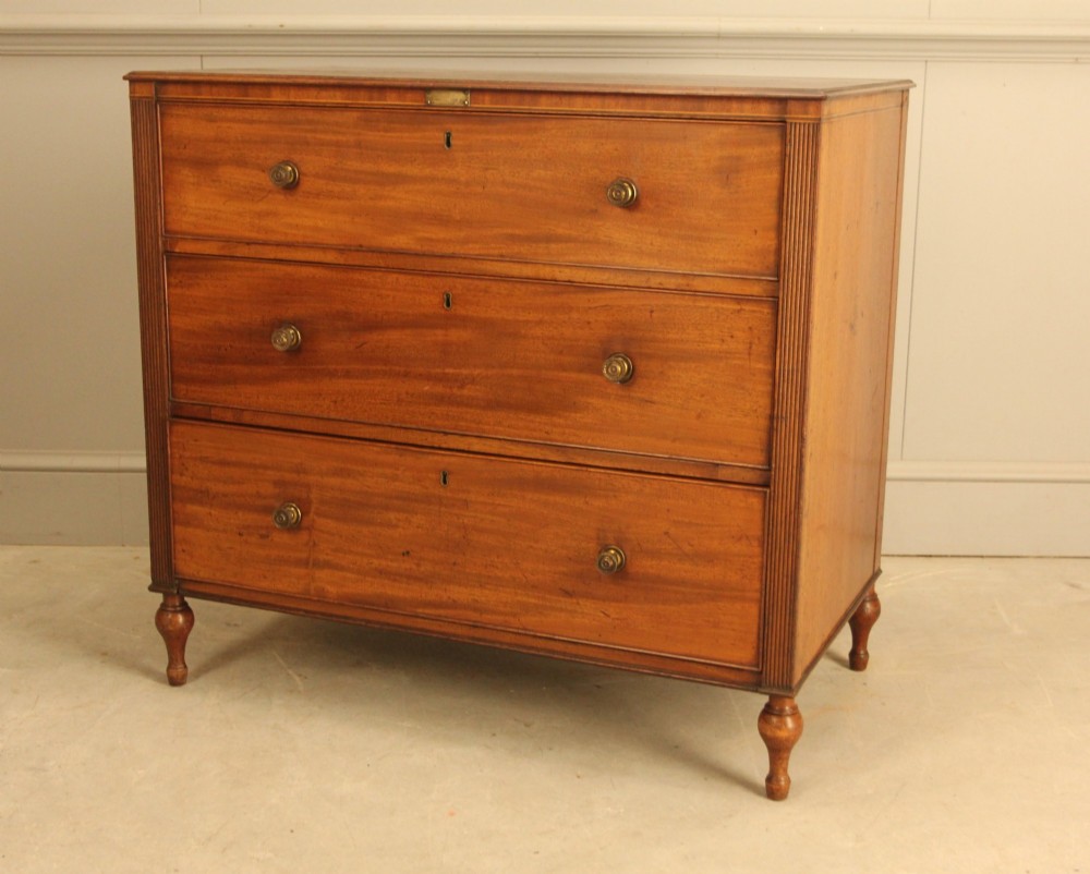 A Regency mahogany chest of drawers featuring three graduated drawers with brass turned knobs and reeded side pilasters resting on turned feet. View III