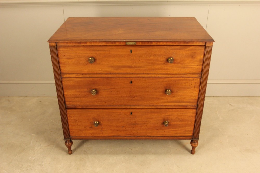 A Regency mahogany chest of drawers featuring three graduated drawers with brass turned knobs and reeded side pilasters resting on turned feet. View IV