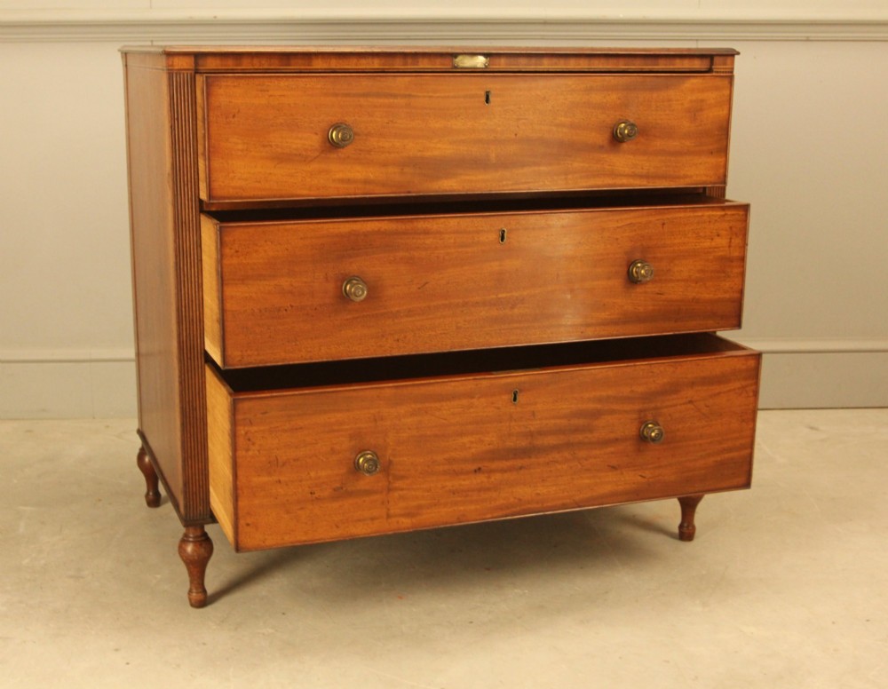 A Regency mahogany chest of drawers featuring three graduated drawers with brass turned knobs and reeded side pilasters resting on turned feet. View V