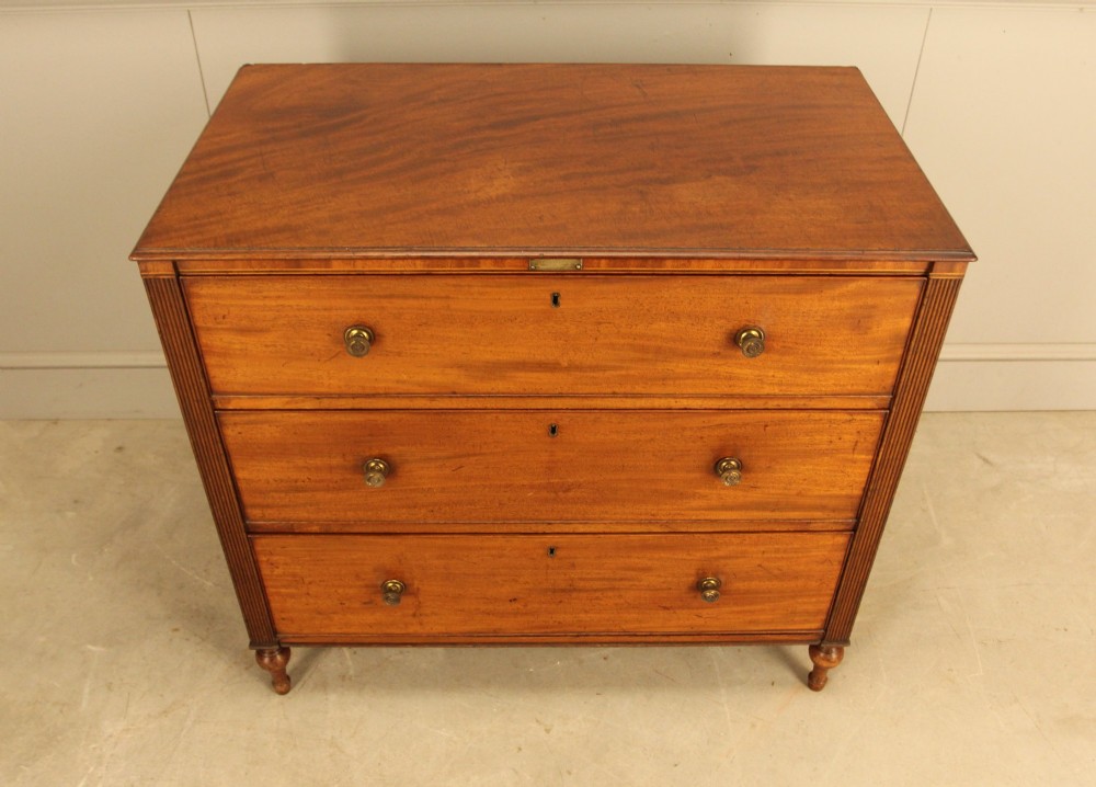 A Regency mahogany chest of drawers featuring three graduated drawers with brass turned knobs and reeded side pilasters resting on turned feet. View VI