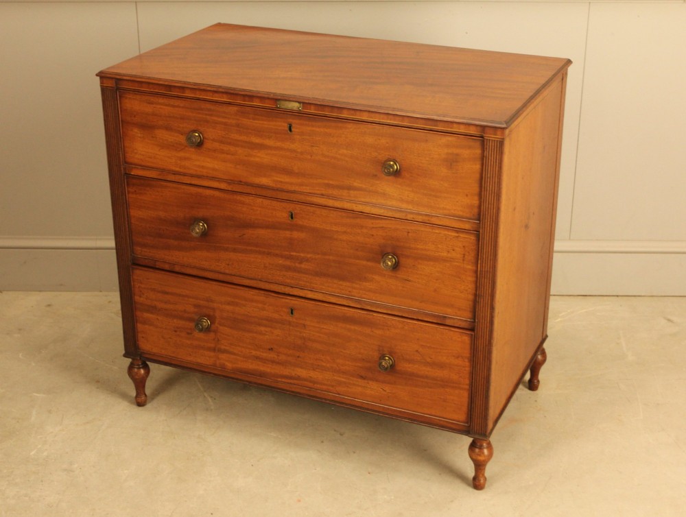 A Regency mahogany chest of drawers featuring three graduated drawers with brass turned knobs and reeded side pilasters resting on turned feet. View VII