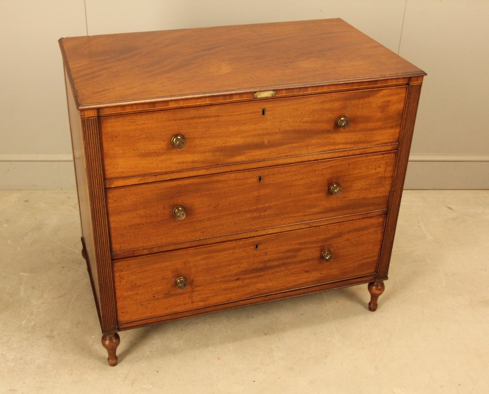 A Regency mahogany chest of drawers featuring three graduated drawers with brass turned knobs and reeded side pilasters resting on turned feet. View VIII