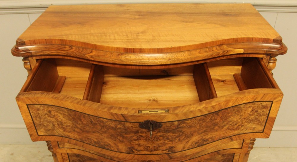 A 19th-century Swedish burr walnut chest featuring four serpentine-front drawers, bookmatched veneers, turned side pilasters, and bun feet. View X