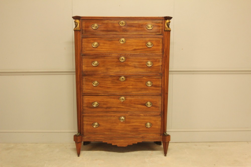 A French 19th-century mahogany tallboy chest of drawers featuring six drawers, brass ring handles, escutcheons, and fluted side pilasters topped with brass busts.